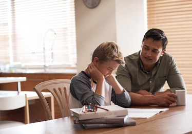 A child crying while doing homework and his dad helps.