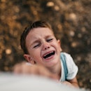 A boy throwing a tantrum and reaching up at their parent, toward the camera.