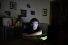 一个白人男孩在黑暗中玩电脑游戏。