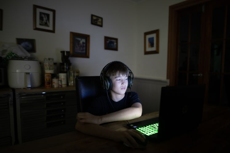 A white boy in the dark playing video games on a computer.