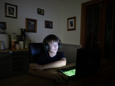A white boy in the dark playing video games on a computer.