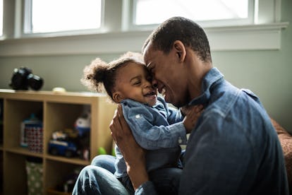 A dad holding his daughter and pressing his face against hers as they both laugh.