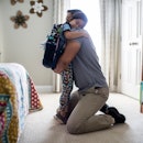 A girl wearing a backpack in her bedroom at home hugs her dad.