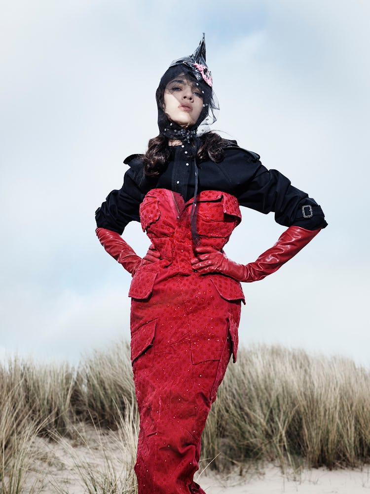 Model wears a red dress, long red leather gloves, hat and black trenchcoat.