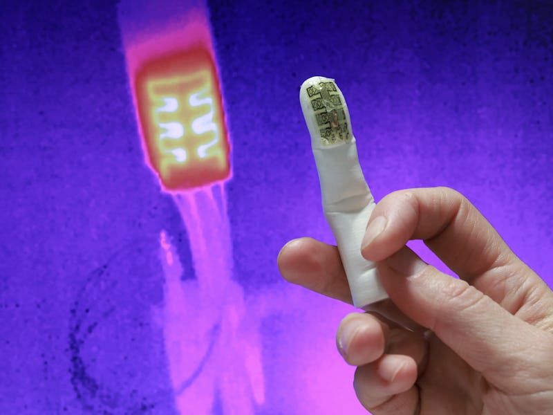 A hand holding a prosthetic finger on a thermal background.