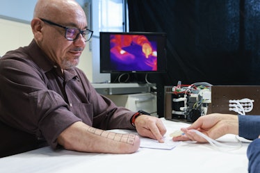 A man with glasses and a shaved head points to a diagram of a hand.