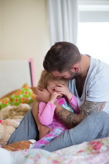 A calm dad comforts his crying daughter with a hug.