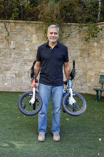 George Clooney standing in a yard holding two children's bicycles