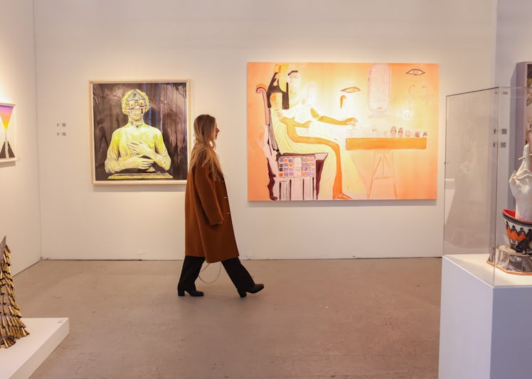a woman walking through an art fair booth featuring figurative paintings