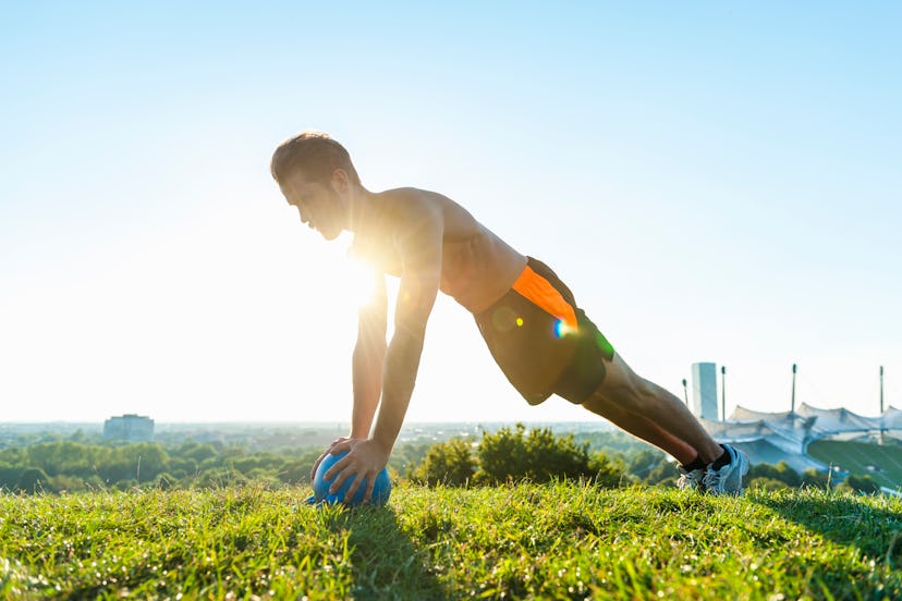 A man in a meadow doing push-ups on a medicine ball.