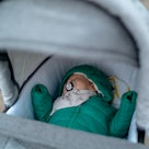A baby win a winter jacket sleeping outdoors in a stroller.