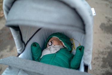 A baby win a winter jacket sleeping outdoors in a stroller.