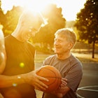 Four older men talk while playing basketball on a court.