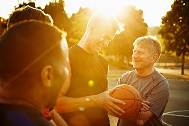 Four older men talk while playing basketball on a court.