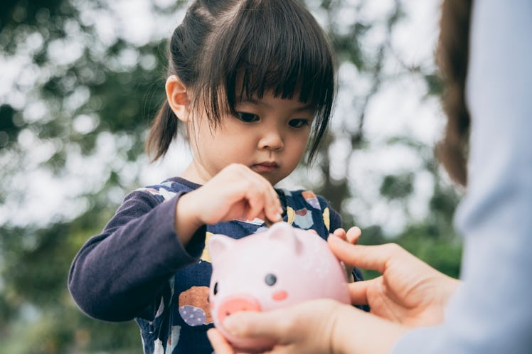 A girl putting change in a piggy bank being held out to her.