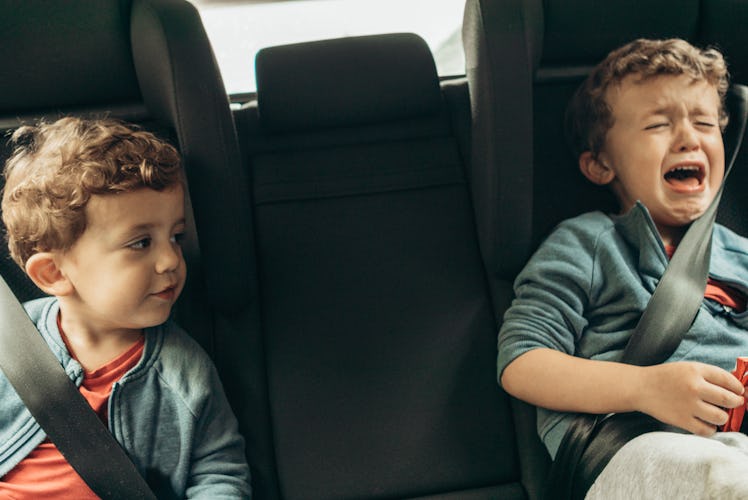 Two boys sitting in the backseat of a car, one having a tantrum.