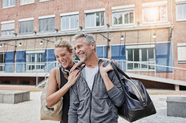 An older man and younger woman flirting outside of a gym.