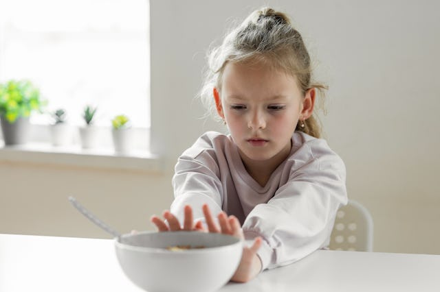 A little girl pushes away a bowl of food.