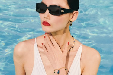 a model wearing dark glasses, gold and gemstone jewelry and a white swimsuit