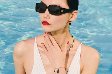 a model wearing dark glasses, gold and gemstone jewelry and a white swimsuit