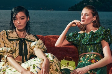 two models wearing floral dresses and sitting on a boat