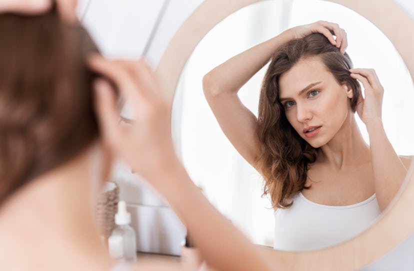 young woman touching her scalp while looking in the mirror
