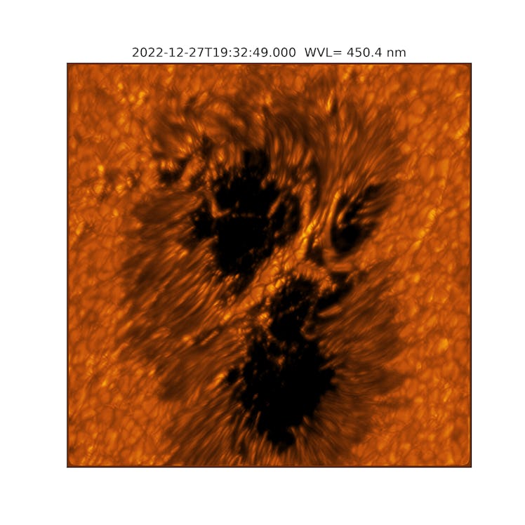 A dark sunspot framed by a bunch of glowing filaments and a bridge of light crossing over the center