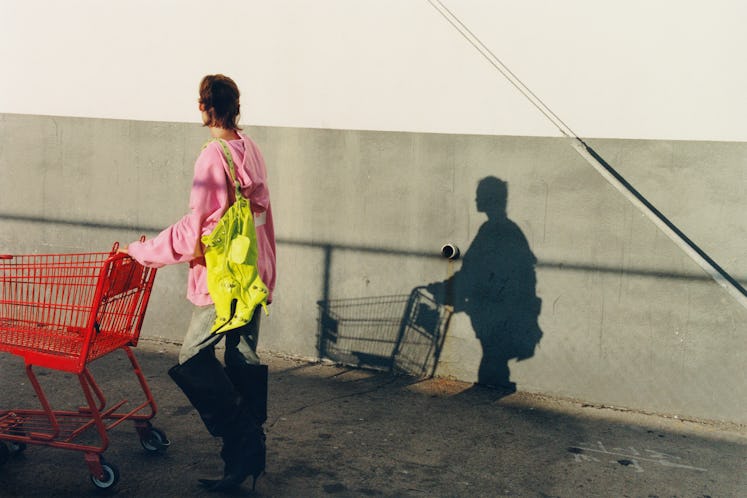A model wearing a pink sweatshirt walks away from the camera pushing a red shopping cart, her late-a...