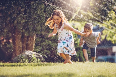 A young girl and boy run through a sprinkler on a summer day