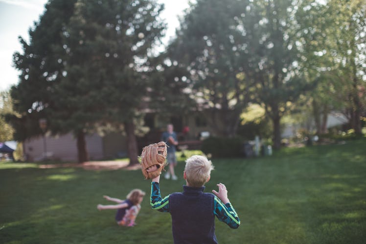 The back of a boy with a baseball glove playing baseball with his family in a backyard