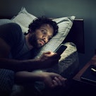 A man checking the time on his phone while in bed at night.
