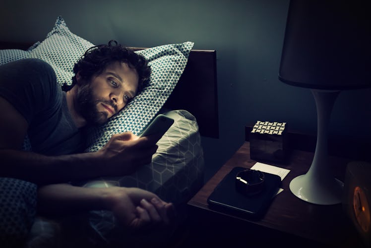 A man checking the time on his phone while in bed at night.