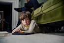 一个男孩在平板电脑上,半躺在父母正坐在沙发上。