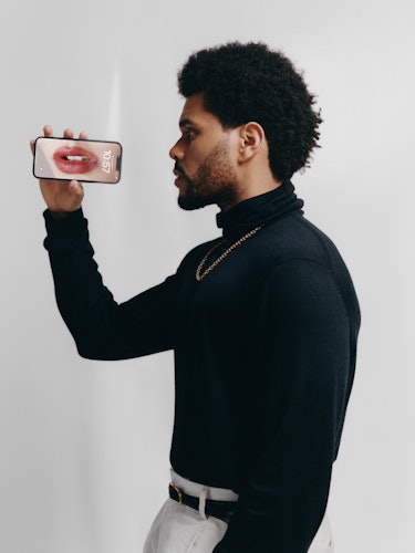 The Weeknd wears a black turtleneck shirt, gold chain necklace, white pants and black leather belt.