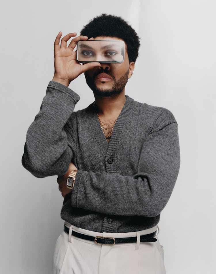 Singer The Weeknd wears a gray cardigan, necklace, gold watch, white pants and black leather belt.