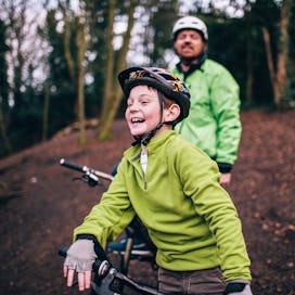 A boy and his dad mountain biking in the woods.