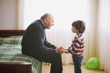 A child holding hands with and listening to his grandfather, who is sitting on the edge of a bed.