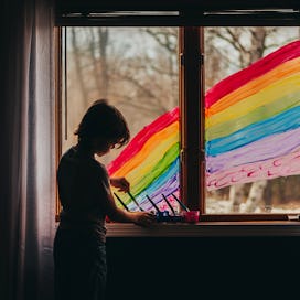 A child painting a large rainbow on the window of their house.