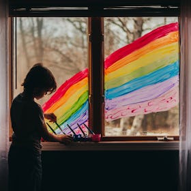 A child painting a large rainbow on the window of their house.
