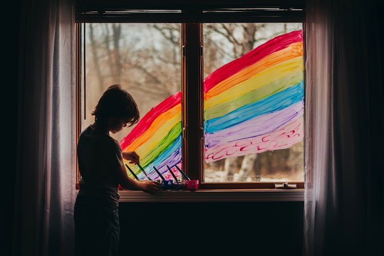 A child painting a large rainbow on the window of their house.