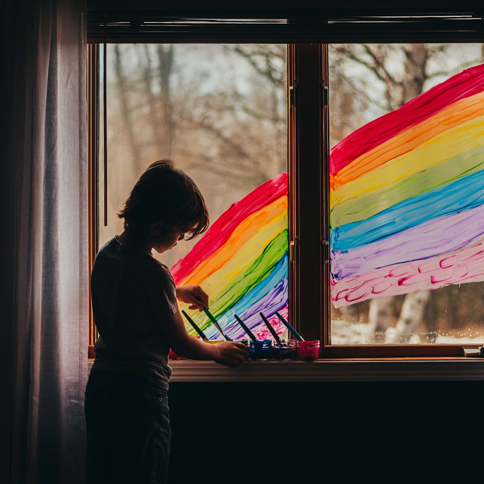 A child painting a large rainbow on the window of their house.