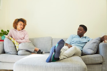 Couple sitting on opposite ends of couch looking annoyed at one another