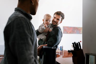 Two dads in a kitchen, one holding their baby.