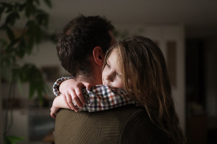 A dad and daughter hugging, looking serious.