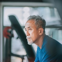 Middle aged man with grey goatee sitting contemplatively in a gym