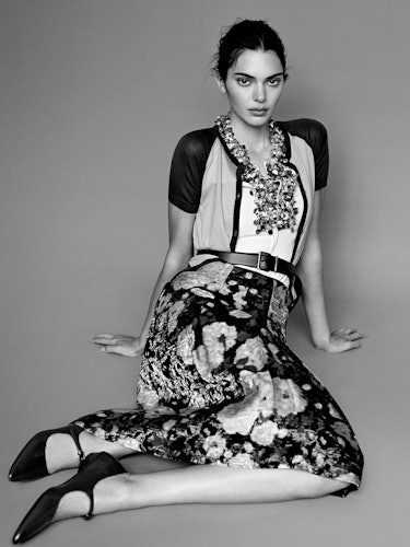 Kendall Jenner wears a floral printed skirt, bulky necklace, sheer cardigan, white shirt, belt and s...