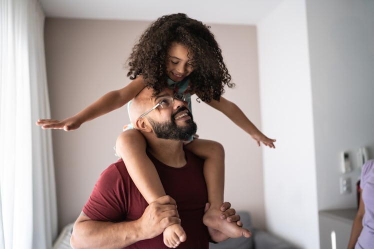 A girl sitting on her dad's shoulders, smiling down at him.