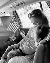 Meghan Markle and Archie ride in the back of a car. Archie carries an American flag.