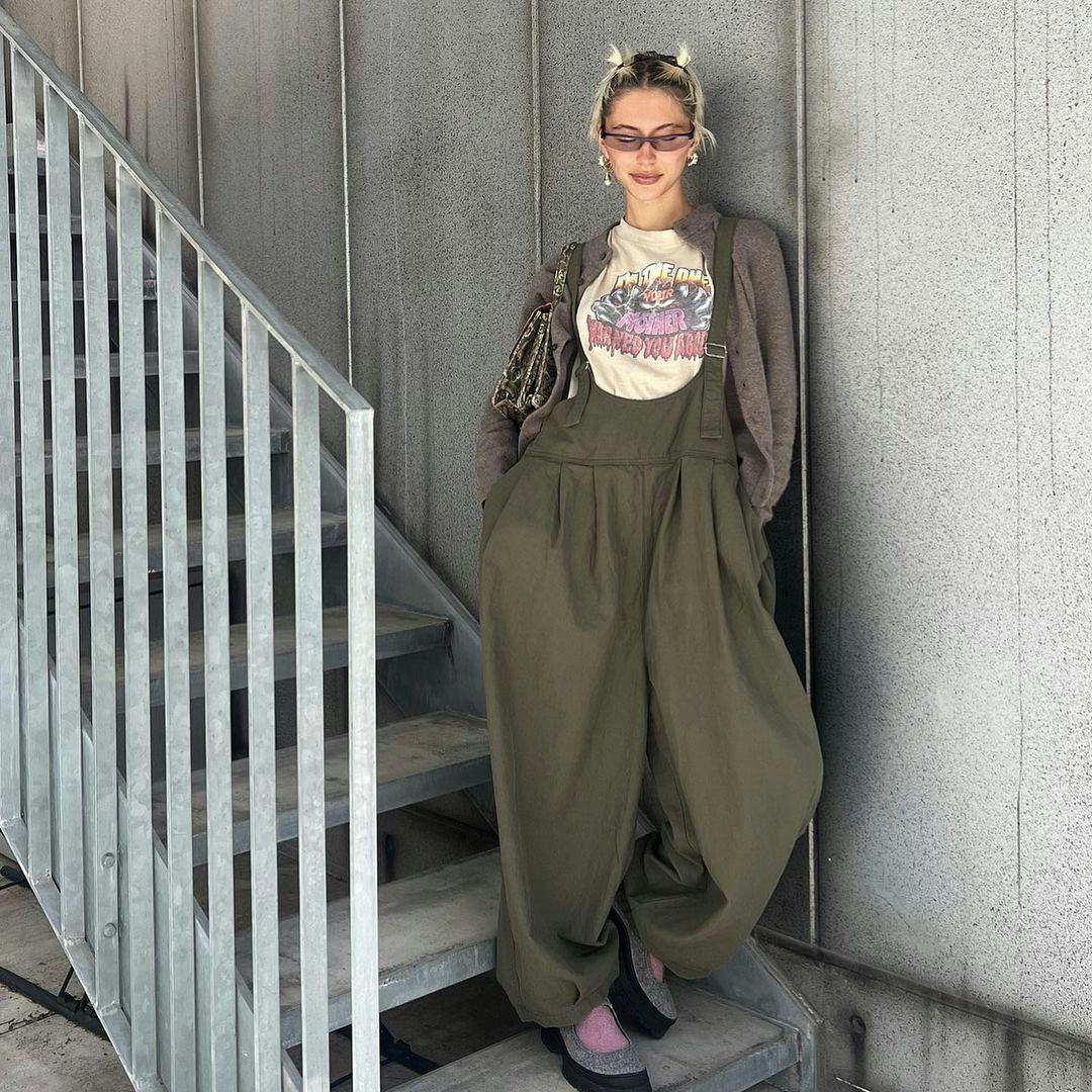 Iris Law wears a green jumpsuit, graphic t-shirt, and brown cardigan in Instagram post.