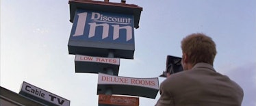 A man with a Polaroid camera photographs a hotel sign that reads "Discount Inn"
